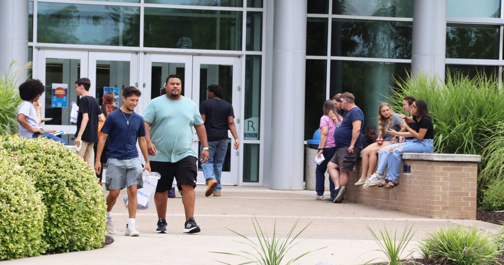 A group of students walks out of Houff Student Center while another group sits on the low wall to one side