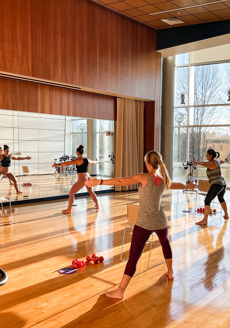 fitness instructor and class participants on sunlit wood floor in front of a large mirror
