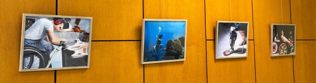Four framed pictures of various folks using prostheses or wheelchairs in various activities