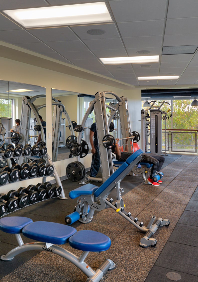 free weights and strength training benches. A student and a spotter near a large window.