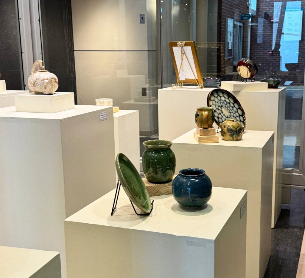 Three dark pots on a stand, behind which are a light teapot and a large patterned plate